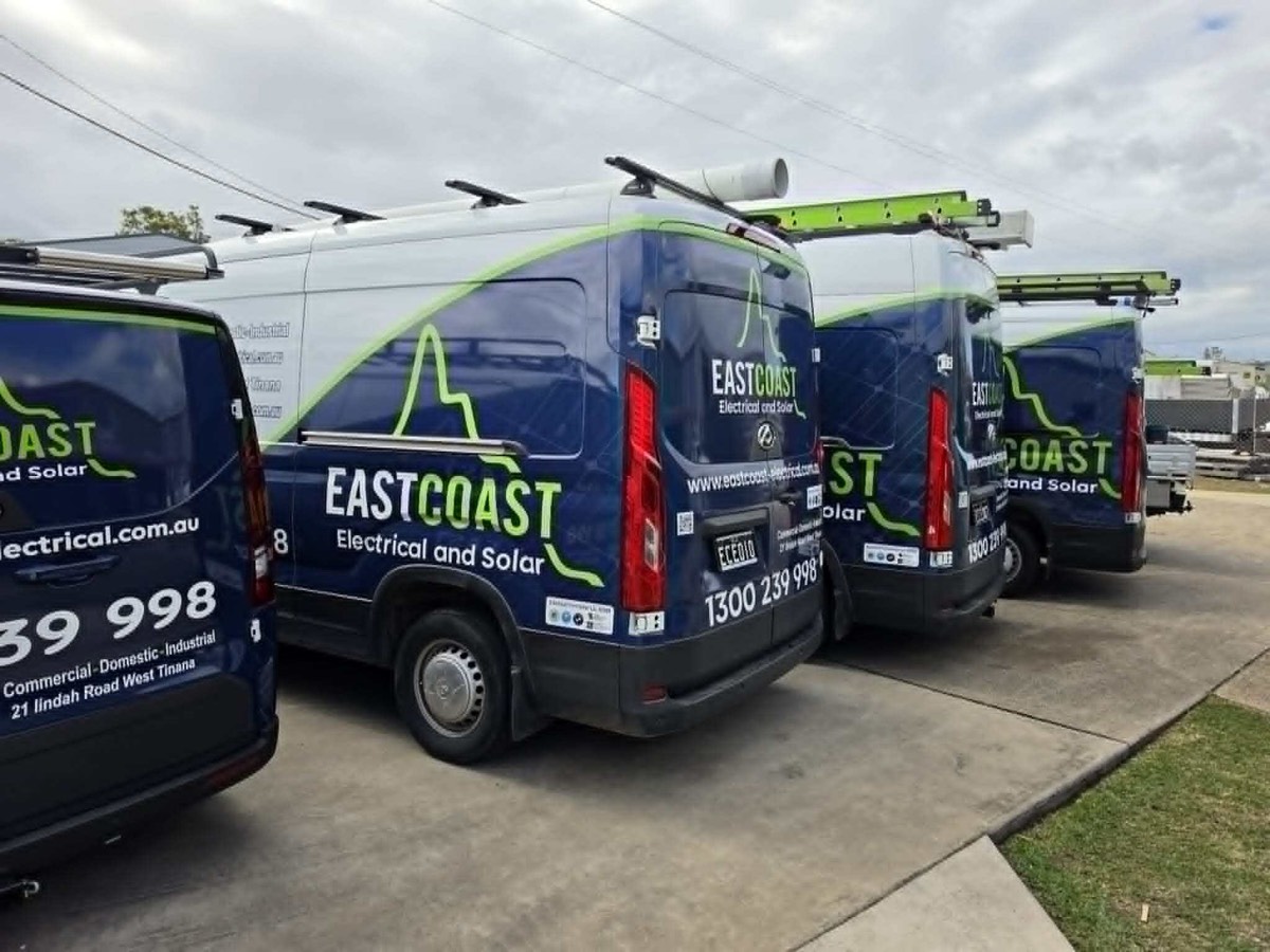 Three branded East Coast Electrical and Solar vans parked at the depot, ladders and conduit on the roof racks