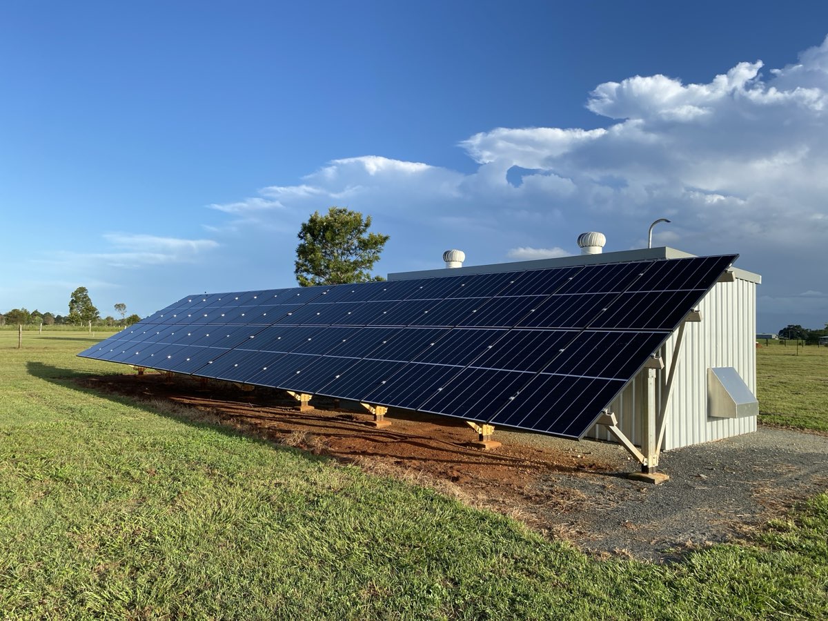 A completed ground-mounted solar array beside a rural shed under clear sky